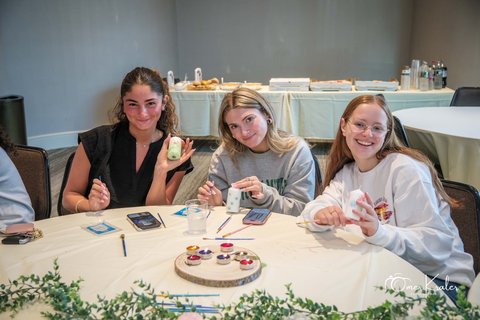 Three friends paint colorful candles around a table.